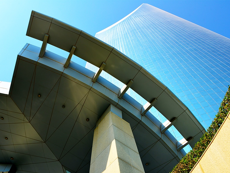 Modern skyscraper with curved glass facade and column-supported overhang against blue sky.